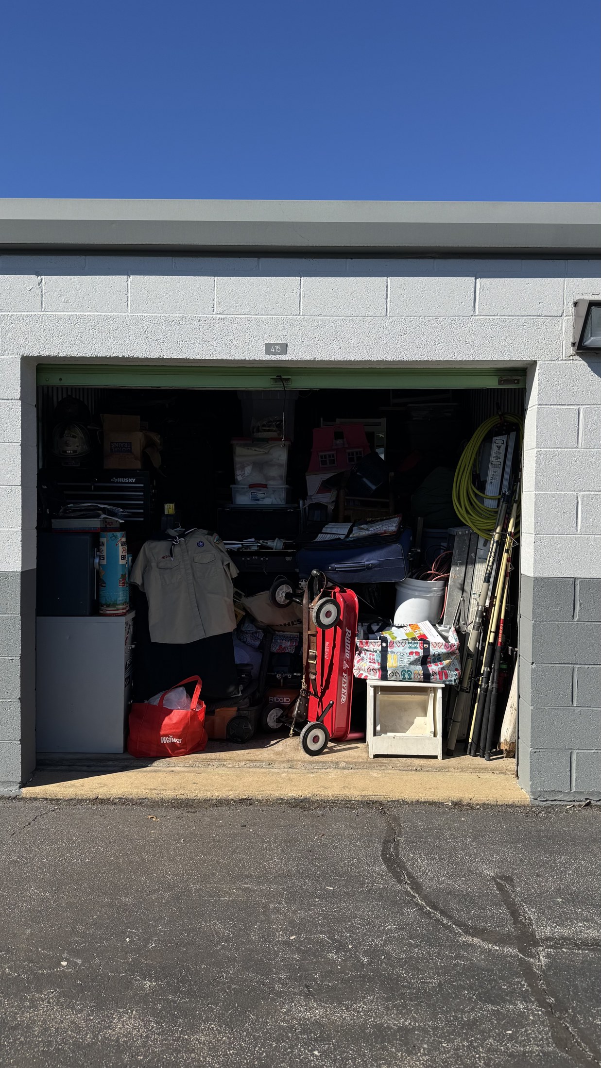 An open storage unit containing boxes, furniture, tools, a red wagon, and other household belongings.